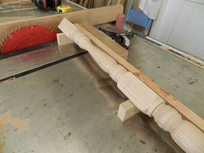 Stool leg positioned on two V blocks to cut six degree tapered cut at top to butt squarely and firmly with the underside of the stool seat