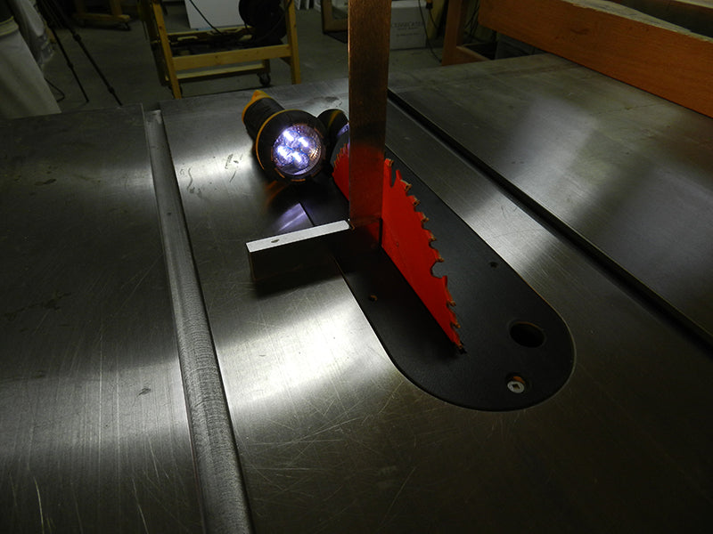 Using a machinist square on the table saw bed to check the saw blade for squareness.
