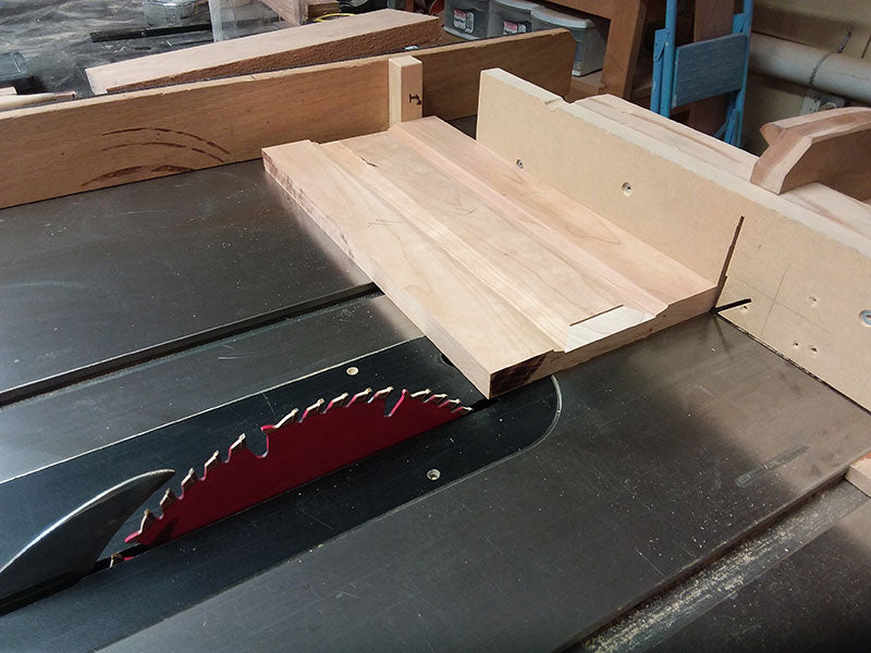 Trimming the rails and center panel used to build the bedside table frame side sections to length in the table saw